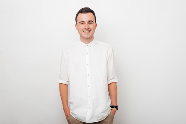 Portrait of a young smiling guy who is holding his hands in his pants pockets on white background.