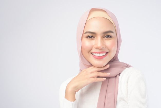 A portrait of young smiling muslim woman wearing a pink hijab over white background studio.