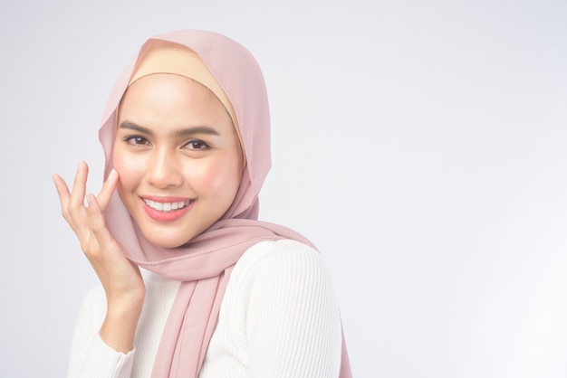 A portrait of young smiling muslim woman wearing a pink hijab on white 