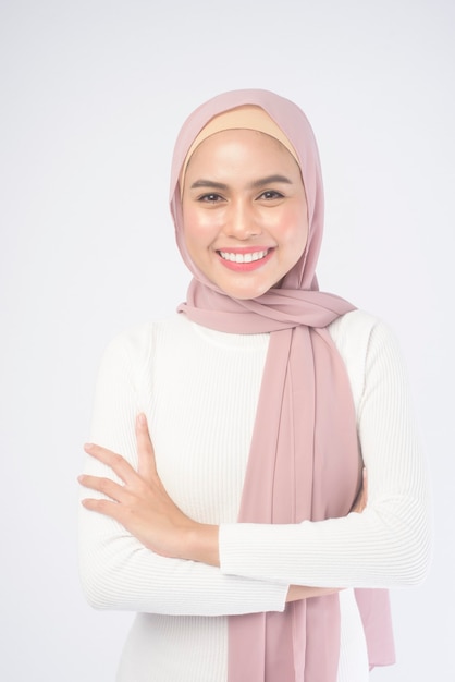 A portrait of young smiling muslim woman wearing a pink hijab on white.