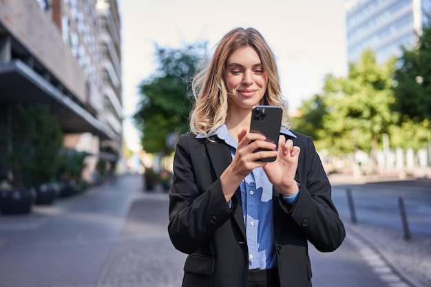 Photo portrait of young smiling saleswoman businesswoman looking at her mobile phone with pleased face rea