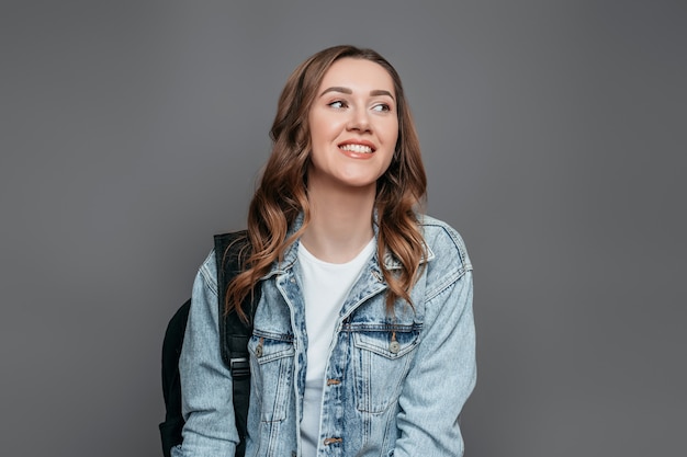 Portrait of a young smiling student girl in a white T-shirt and denim jacket with a backpack