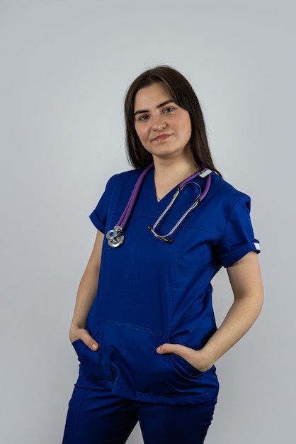 Portrait of young smiling woman nurse or student in blue uniform with stethoscope isolated ob grey