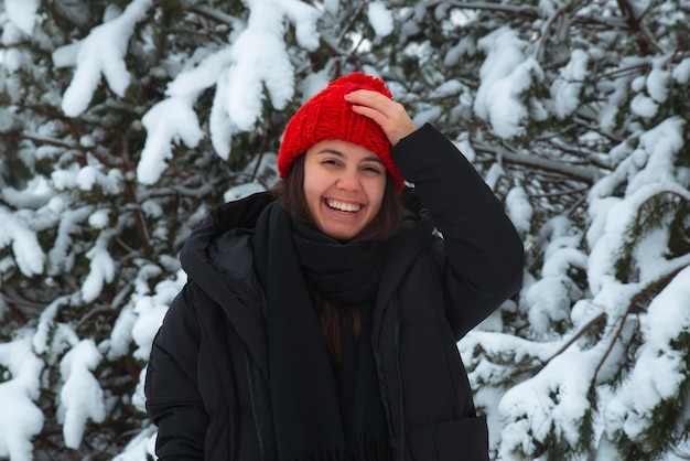 Portrait of young smiling woman in winter clothes in red hat with bubo fir tree in background