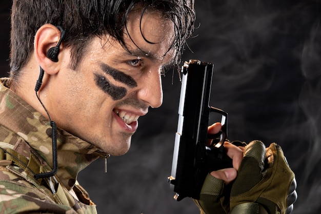 Portrait of young soldier in camouflage holding gun on black wall