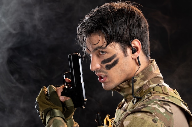 Portrait of young soldier in camouflage holding gun on black wall