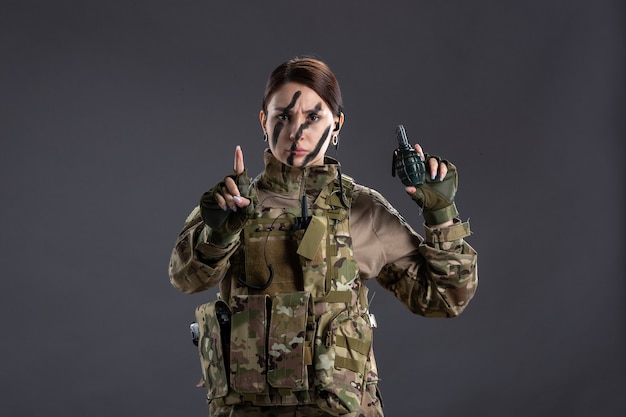 Portrait of young soldier in camouflage with grenade on her hands dark wall