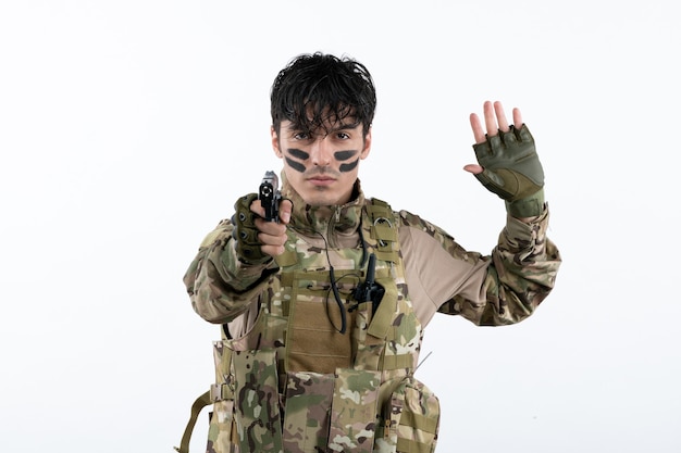 Portrait of young soldier in camouflage with gun on white wall