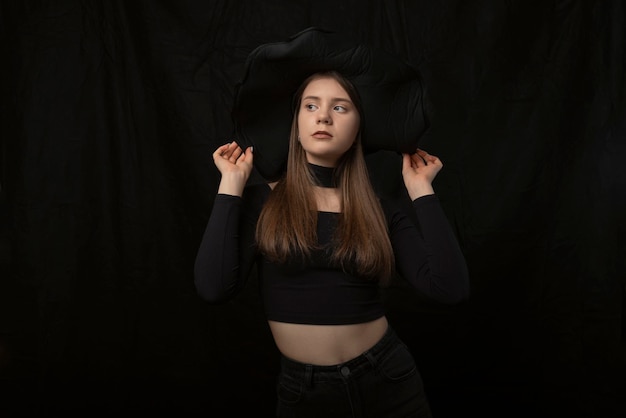 Portrait of young stylish girl in short tightfitting top and widebrimmed hat in the studio Black background