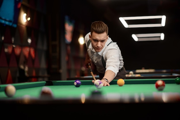 Portrait of young stylish man preparing for game rubbing pool cue stick at billiards club