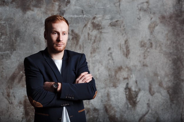 Portrait of a young successful leader. His red hair is neatly trimmed. He is dressed in a classic dark suit.