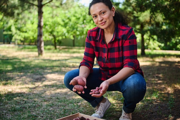 Portrait of a young successful woman gardener agronomist with fresh crop of organic potatoes smiling looking at camera