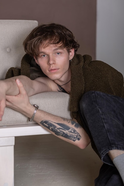 Portrait of a young tattooed guy with earring leaning on the couch