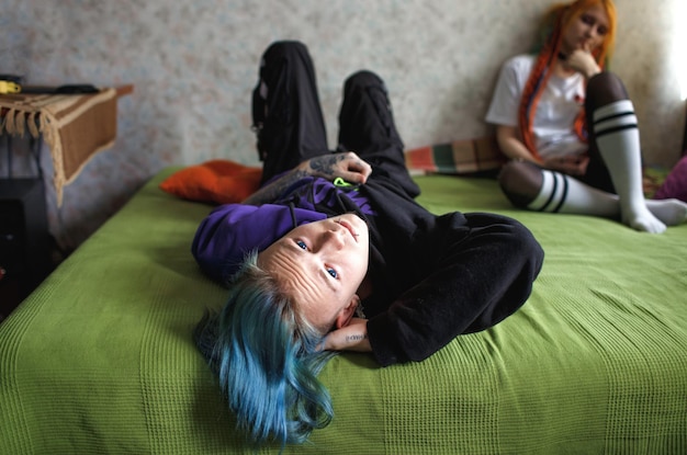 Portrait of a young tattooed guy with long dyed braided hair in a windbreaker lying