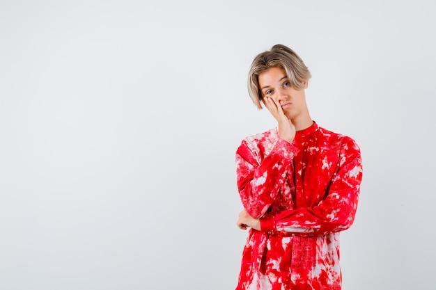 Portrait of young teen boy leaning cheek on hand in shirt and looking sad front view