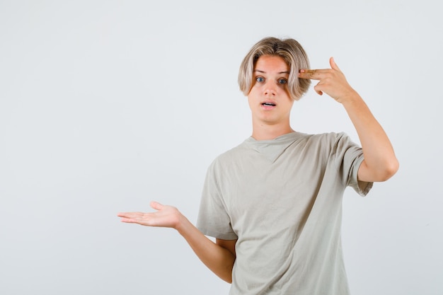 Portrait of young teen boy showing suicide gesture, spreading palm aside in t-shirt and looking bewildered front view