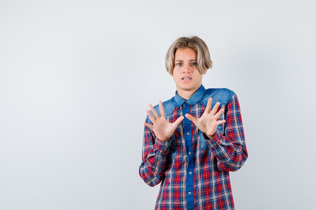 Portrait of young teen boy showing surrender gesture in checked shirt and looking frightened front view