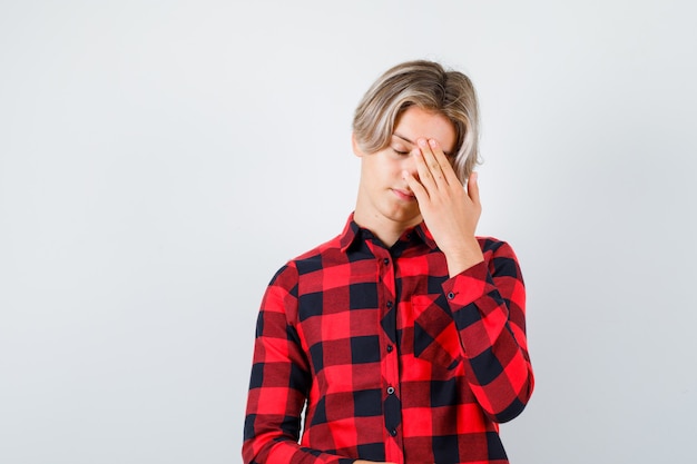 Portrait of young teen boy with hand on head in checked shirt and looking tired front view