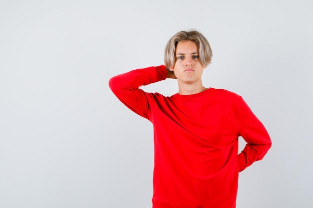 Portrait of young teen boy with hand behind head in red sweater and looking concerned front view