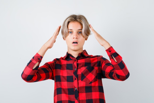 Portrait of young teen boy with hands near head in checked shirt and looking puzzled front view