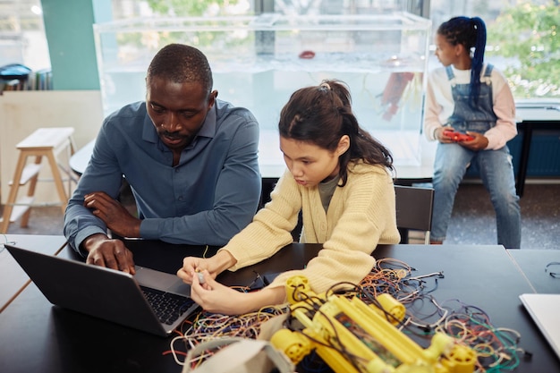 Portrait of young teenage girl building robots in engineering class with male teacher helping