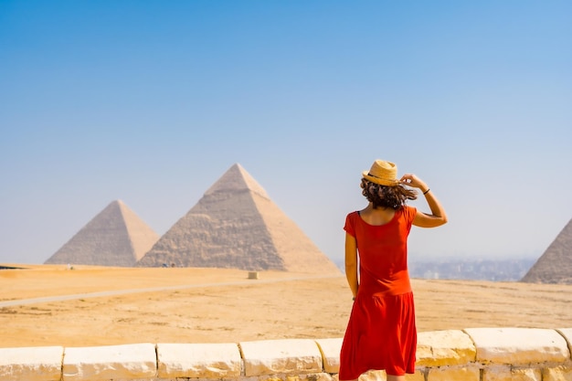 Portrait of a young tourist in red dress enjoying the pyramids of Giza