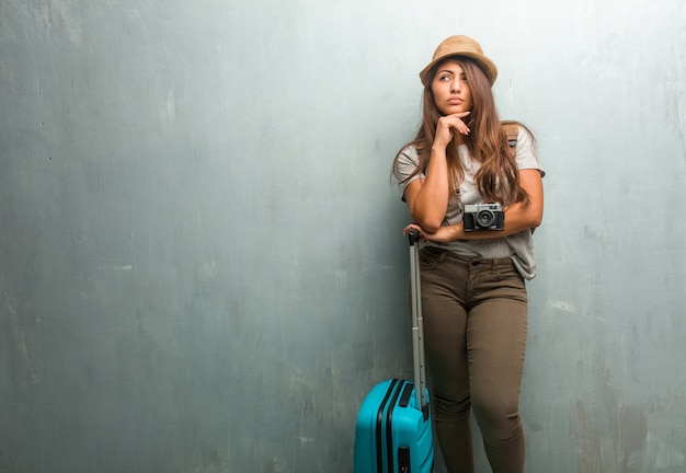 Portrait of young traveler latin woman against a wall thinking and looking up