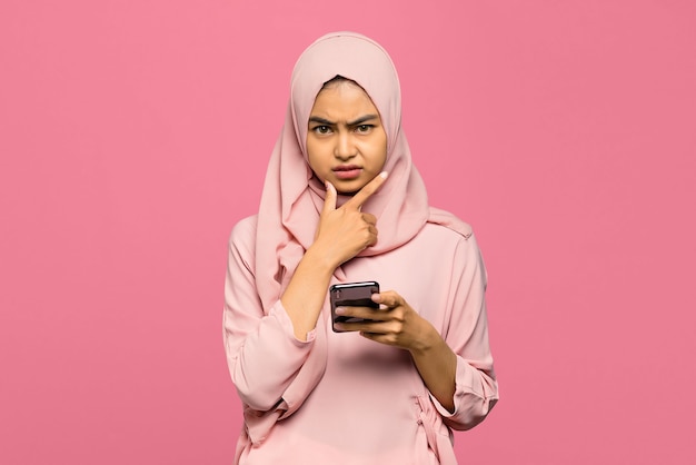 Portrait of young unhappy Asian woman holding mobile phone with confused face