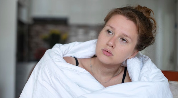 Portrait of young unhappy depressed girl beautiful lazy lonely woman covering herself in blanket