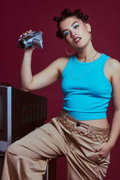 Portrait of young woman in 2000s fashion style posing with television and portable camera