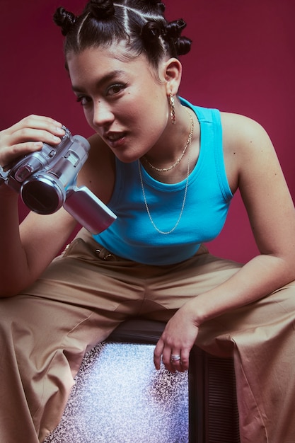 Portrait of young woman in 2000s fashion style posing with television and portable camera