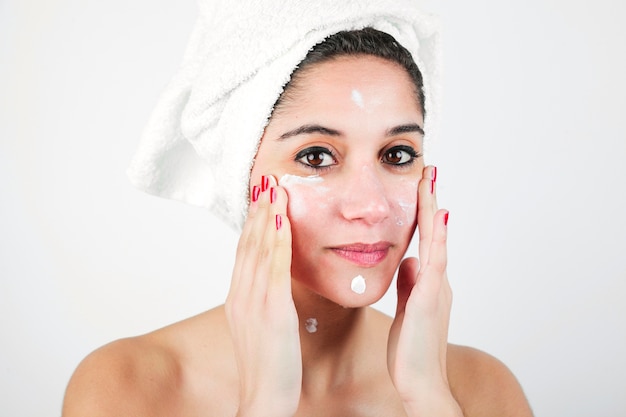 Portrait of young woman applying moisturizer on her face isolated on white background