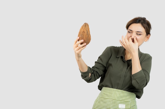 Portrait of young woman in apron holding a coconut and covering nose