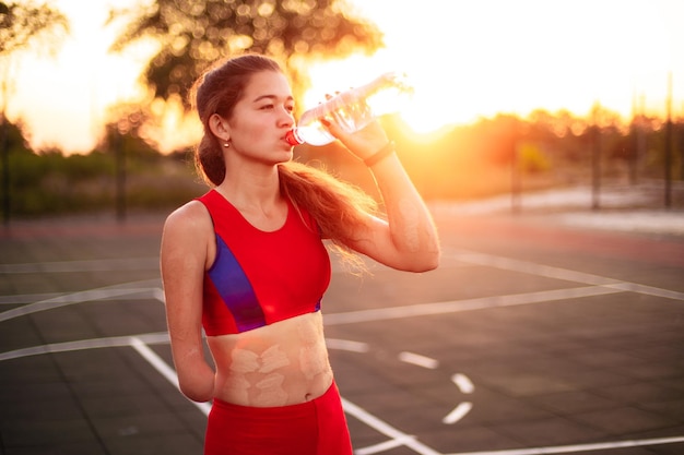 Portrait young woman athlete with an amputated arm and burns on her body She drinks water from a bottle after training outdoors at sunset