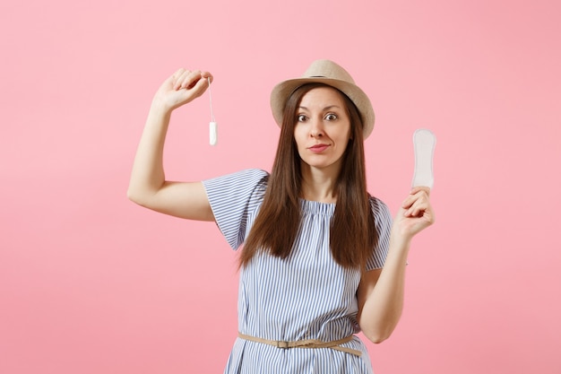 Portrait of young woman in blue dress holding sanitary napkin, tampon for variant safety menstruation days isolated on pink background. Medical healthcare, gynecological, choice concept. Copy space.