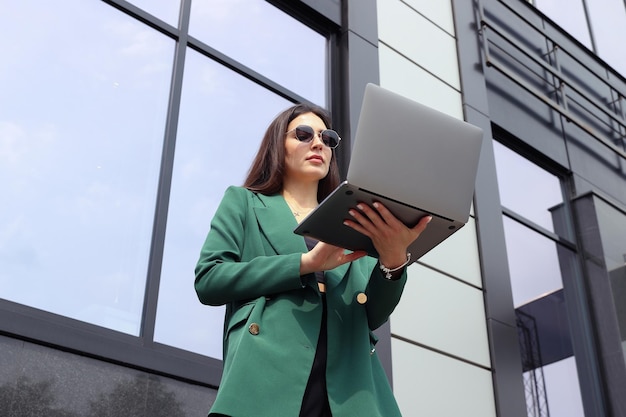 Portrait of a young woman in a business suit with a laptop on the background of buildings