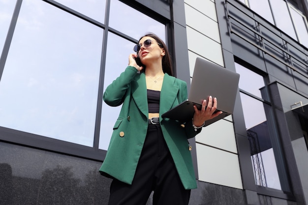 Portrait of a young woman in a business suit with a laptop and a mobile phone