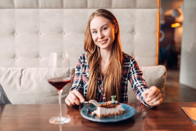 Photo portrait of young woman in cafe, sweet cake and red wine in a glass on the table. girl with chocolate dessert in restaurant