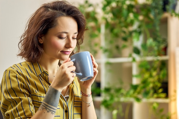 Photo portrait of young woman in casual wear starting her day with a cup of coffee or herbal tea relaxing