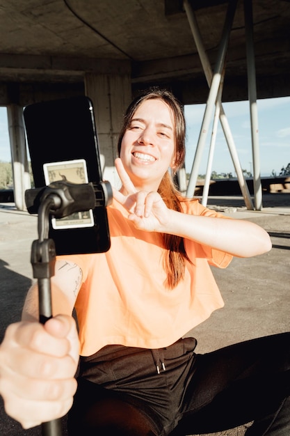 Portrait of young woman content maker starting and recording a shooting greeting with big smile on social networkHolding mobile phone and doing peace symbol checking everything is ok Casual stream