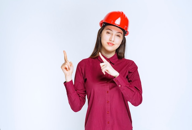 Portrait of young woman in crash helmet pointing up. 