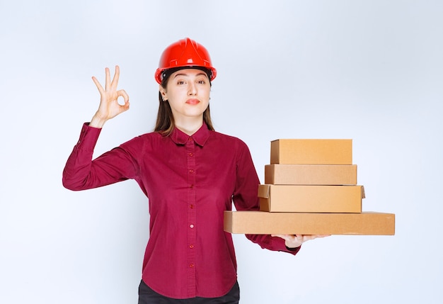 Portrait of a young woman in crash helmet with paper boxes showing ok gesture . 