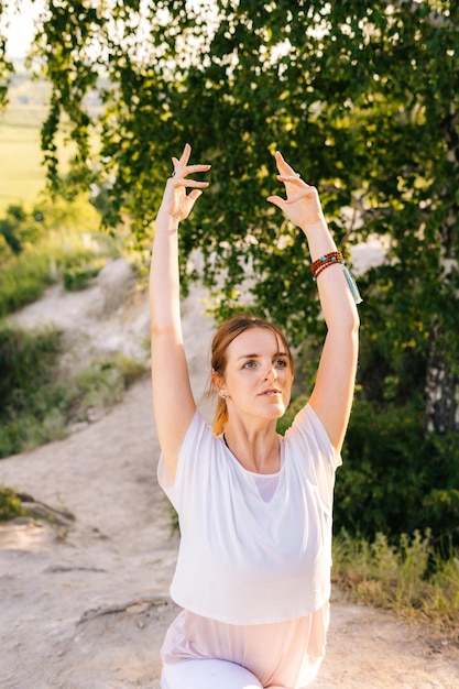 Portrait of young woman doing warrior yoga asana pose on top of rock background of landscape