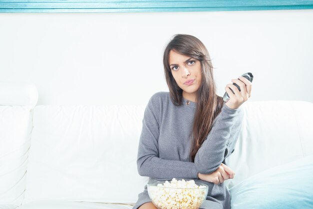 Portrait of a young woman eating popcorn while watching TV at home