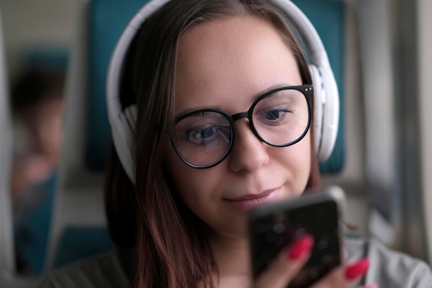 Portrait of young woman in glasses browsing mobile phone riding on train Close up Pretty female using gadget while sitting in suburban train