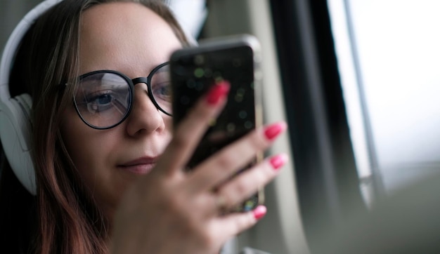 Portrait of young woman in glasses browsing mobile phone riding on train Close up Pretty female using gadget while sitting in suburban train