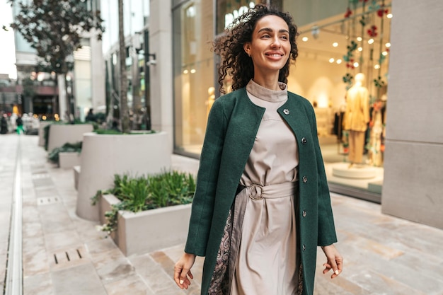 Portrait of young woman in green coat with curly hair in the city