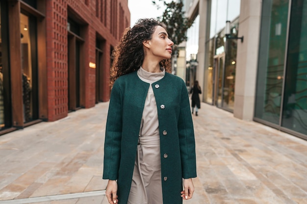 Portrait of young woman in green coat with curly hair in the city