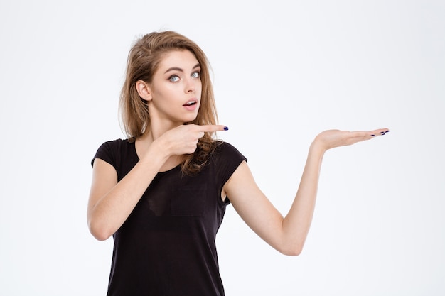 Portrait of a young woman holding copyspace on the palm and pointing finger on it isolated on a white background