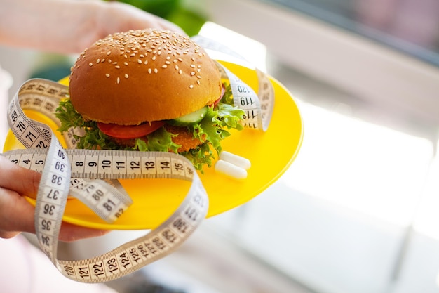 Portrait young woman holding harmful fat burger with white measuring tape